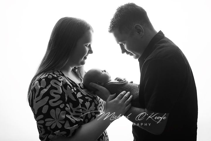 Black and white photo of parents tenderly cradling their newborn baby, captured by Michael O'Keefe Photography.