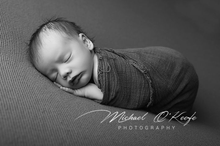 Black and white newborn photography of a sleeping baby wrapped in a soft blanket by Michael O'Keefe Photography.