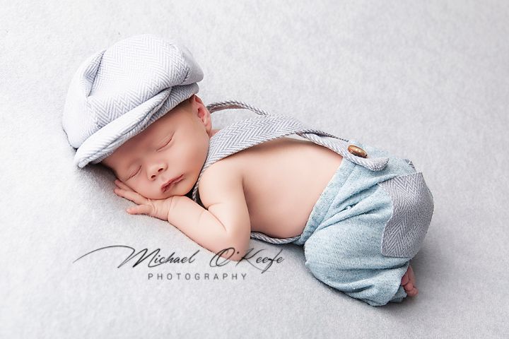 Newborn baby in white hat and light blue wrap lying on soft white blanket in artistic black and white photography.