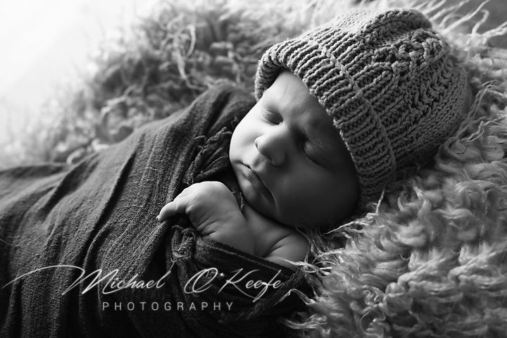 Artistic black and white newborn portrait on soft textured blanket.
