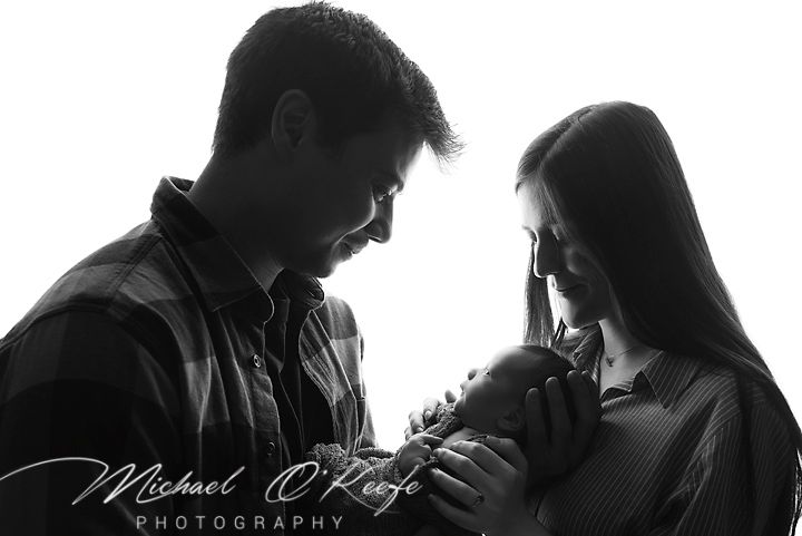 Black and white newborn photo of parents tenderly cradling their baby, studio portrait by Michael O'Keefe Photography.