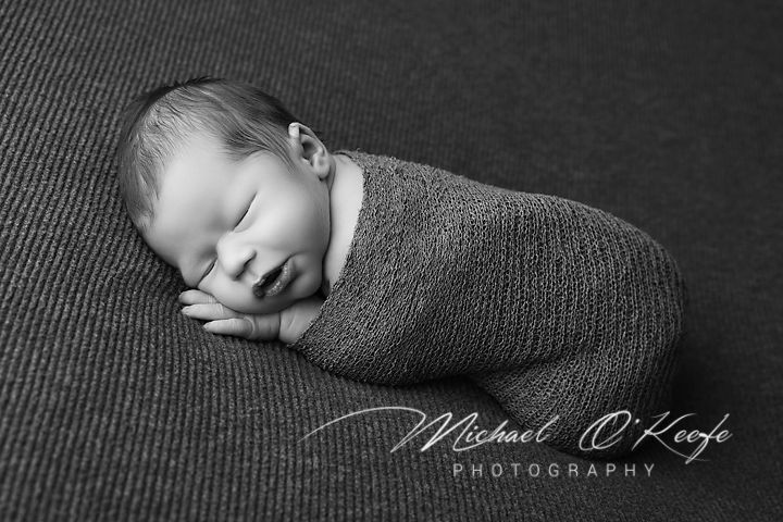 Black and white newborn photography series showing peaceful sleeping baby in various gentle poses on textured fabric.