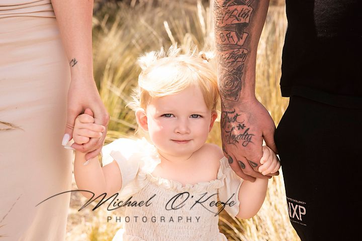 A golden-lit outdoor family portrait session with sunlight streaming through trees creating a warm ethereal atmosphere.