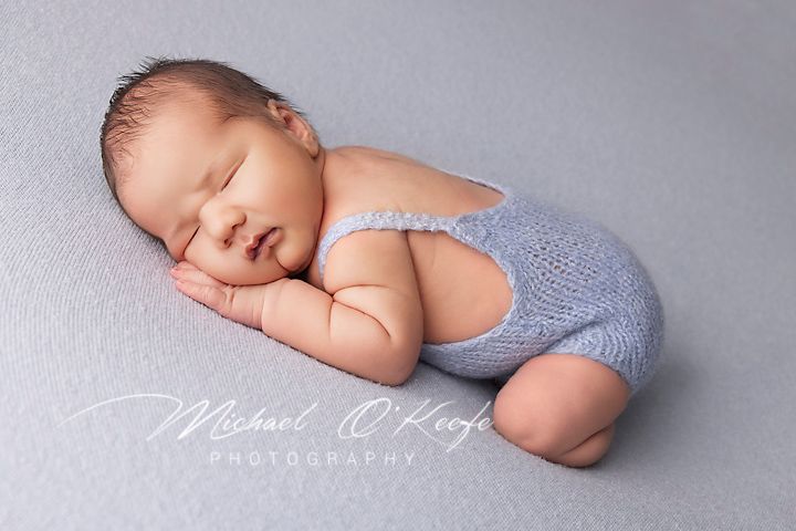 A peaceful newborn baby sleeping in soft gray swaddle blankets during professional photography session.