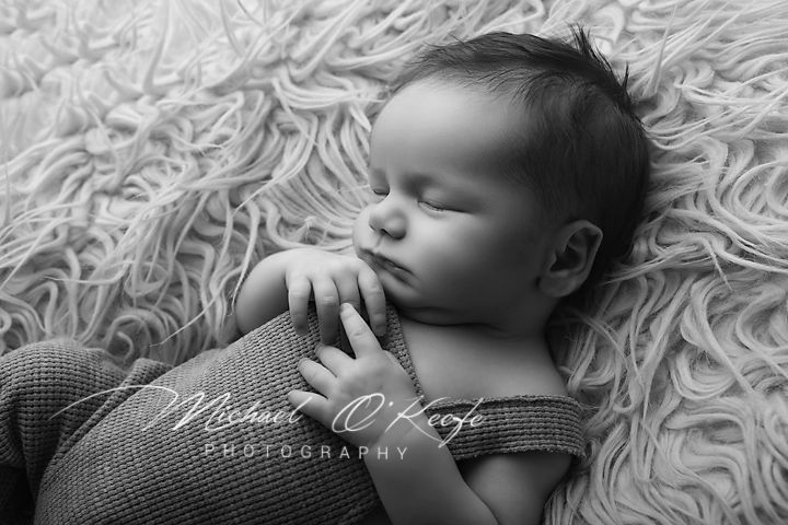 Black and white newborn photography of a sleeping baby with hands clasped, resting on a fluffy textured blanket.