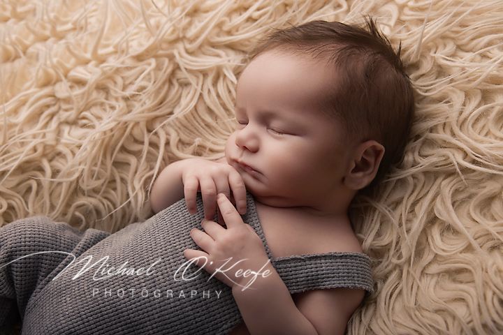 Sleeping newborn baby in gray romper on fluffy beige fur, photographed by Michael O'Keefe Photography.