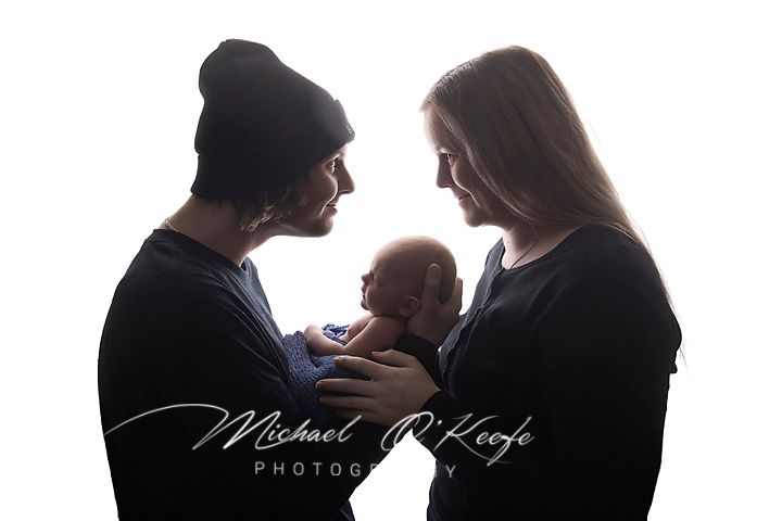 Silhouette of parents holding newborn baby against white background, Michael OKeefe Photography watermark visible.