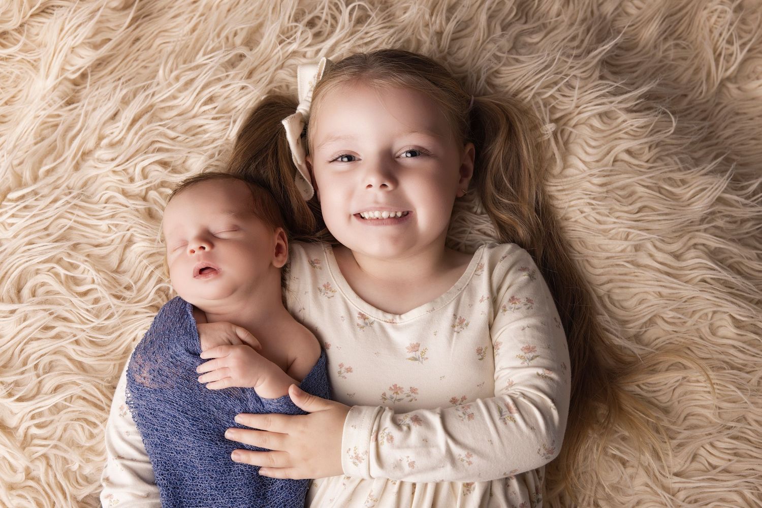 Siblings lying on a fluffy beige rug during an intimate portrait session.
