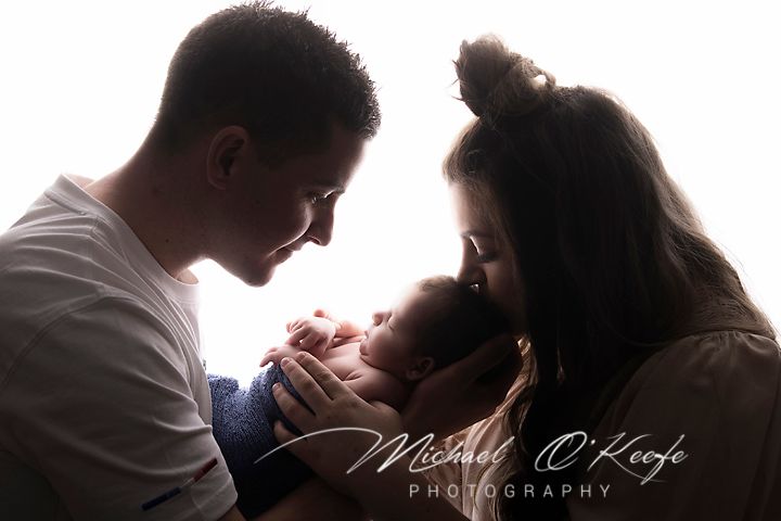 Silhouetted family sharing an intimate moment with newborn in black and white portrait.
