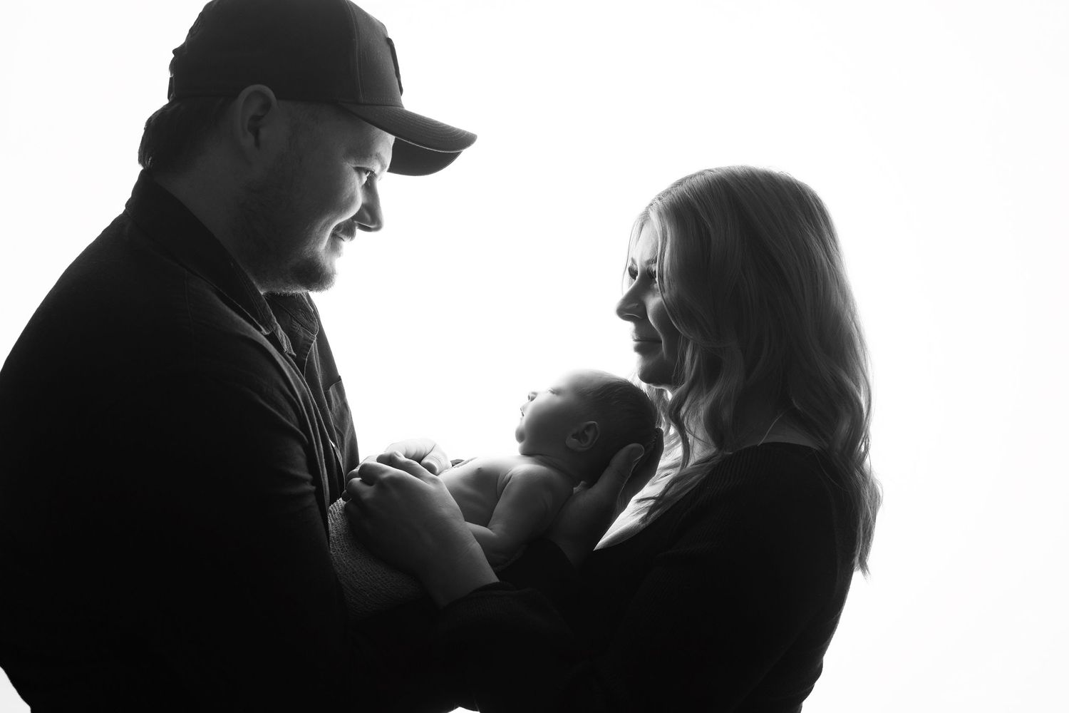 High contrast silhouette portrait series of family with newborn against white background.