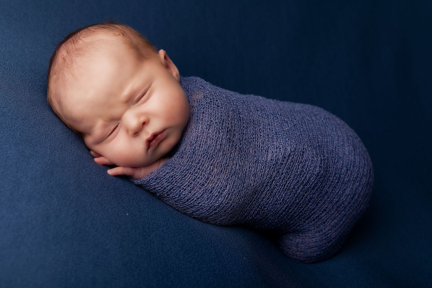 Serene newborn photo against navy background with soft knit wrapping.