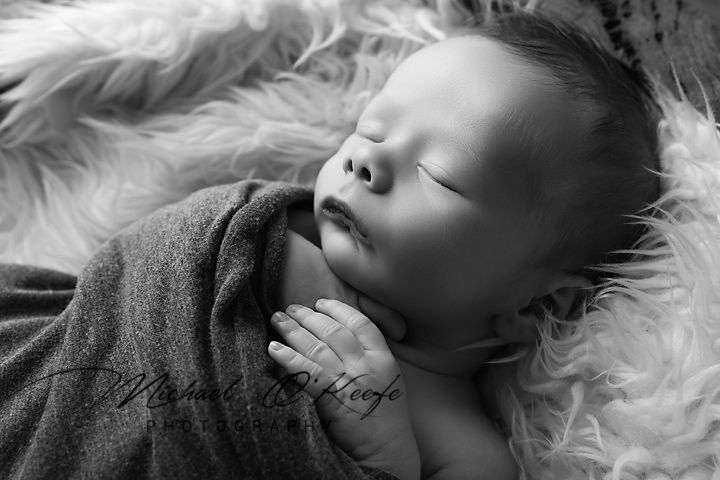 A series of black and white newborn portraits showing sleeping baby on soft white fur background.