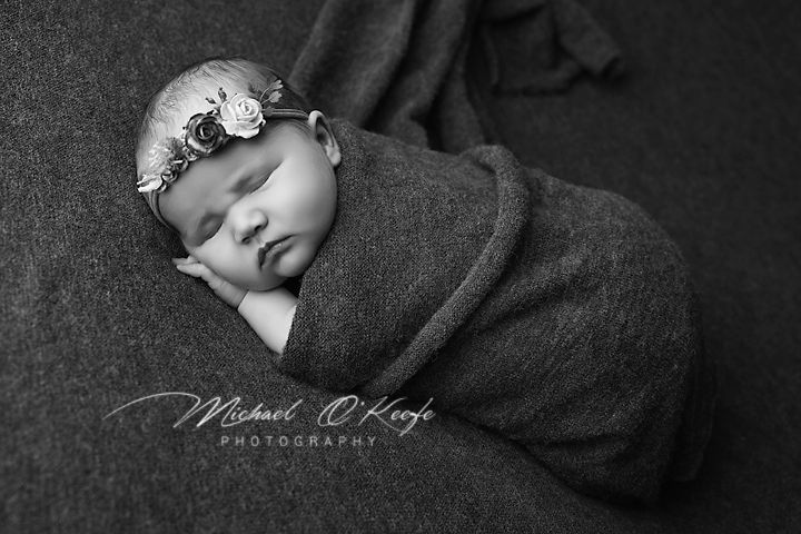 Artistic black and white newborn photography series showing sleeping baby wrapped in dark textured blanket.