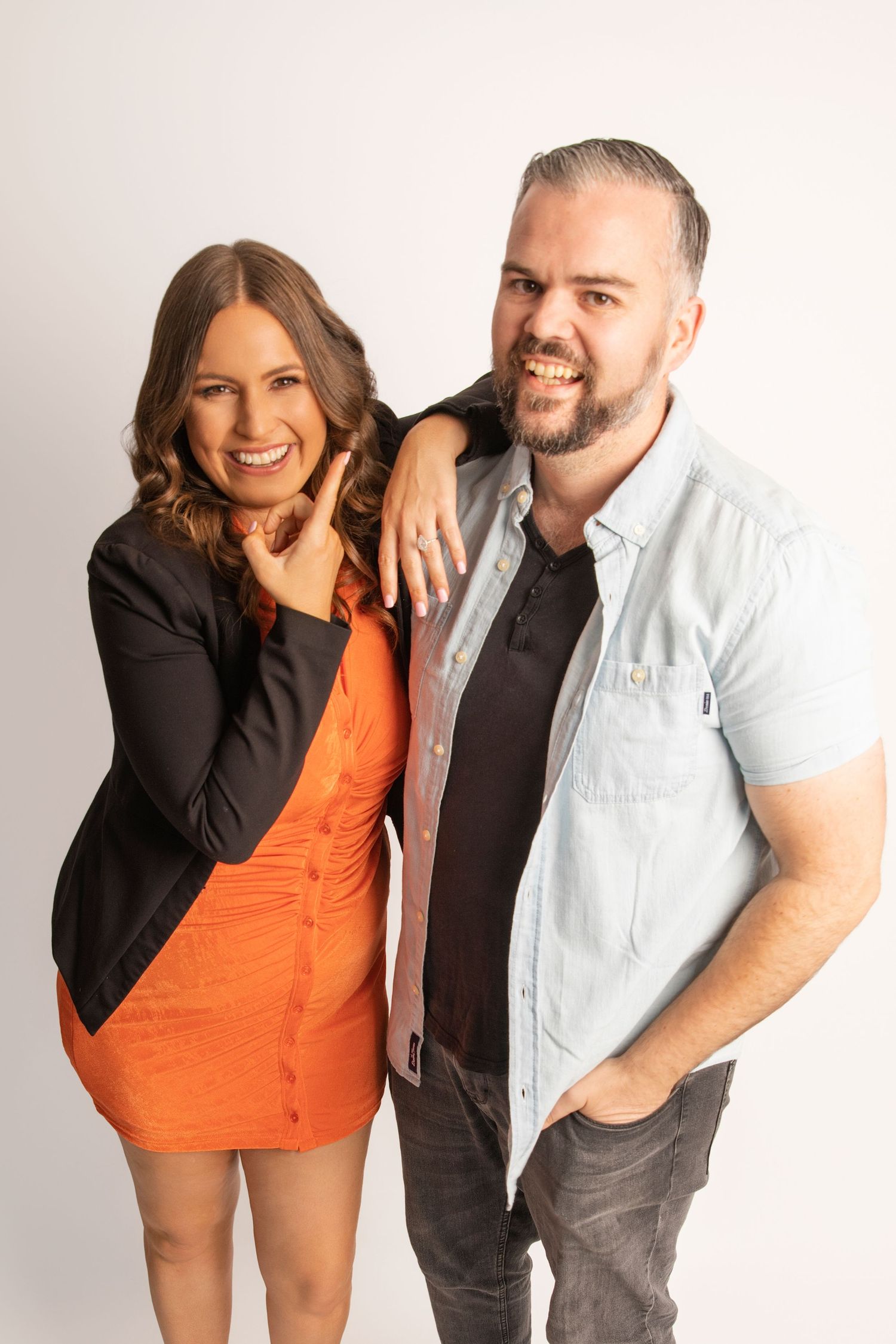 Two people pose together in studio wearing orange and light colored outfits.