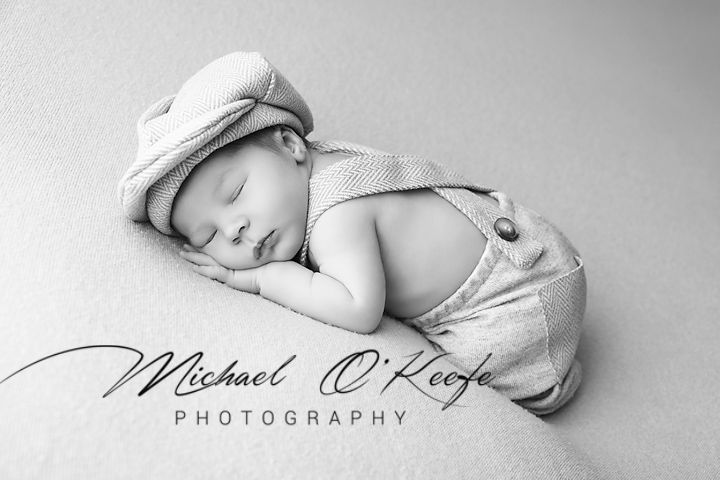 A sleeping baby wrapped in soft white fabric lies peacefully in a black and white photograph.