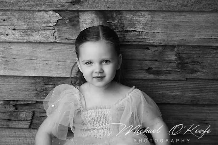 Artistic black and white panoramic sequence showing a child in white dress sitting against rustic wooden planks.