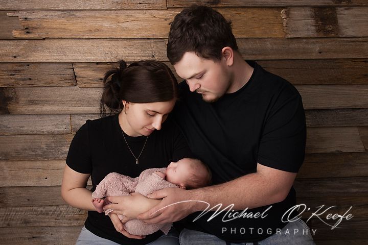 New parents in black shirts tenderly cradle their sleeping newborn baby in a professional studio portrait.