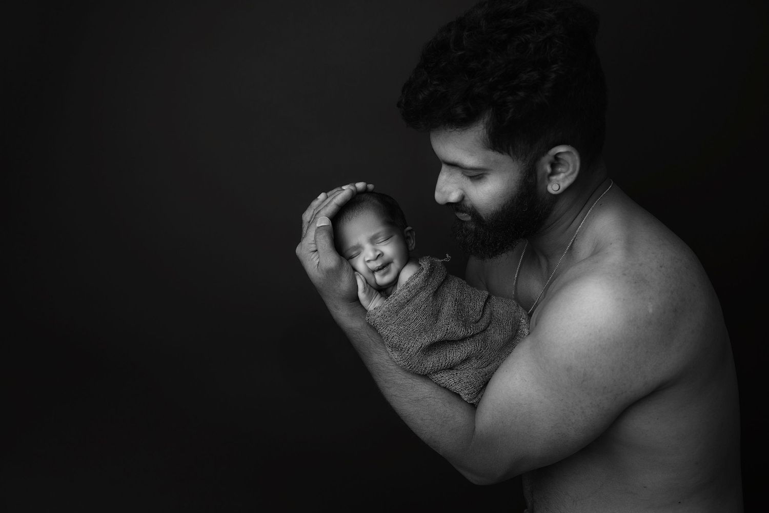 Black and white portrait of tender moment between parent and baby against dark background.