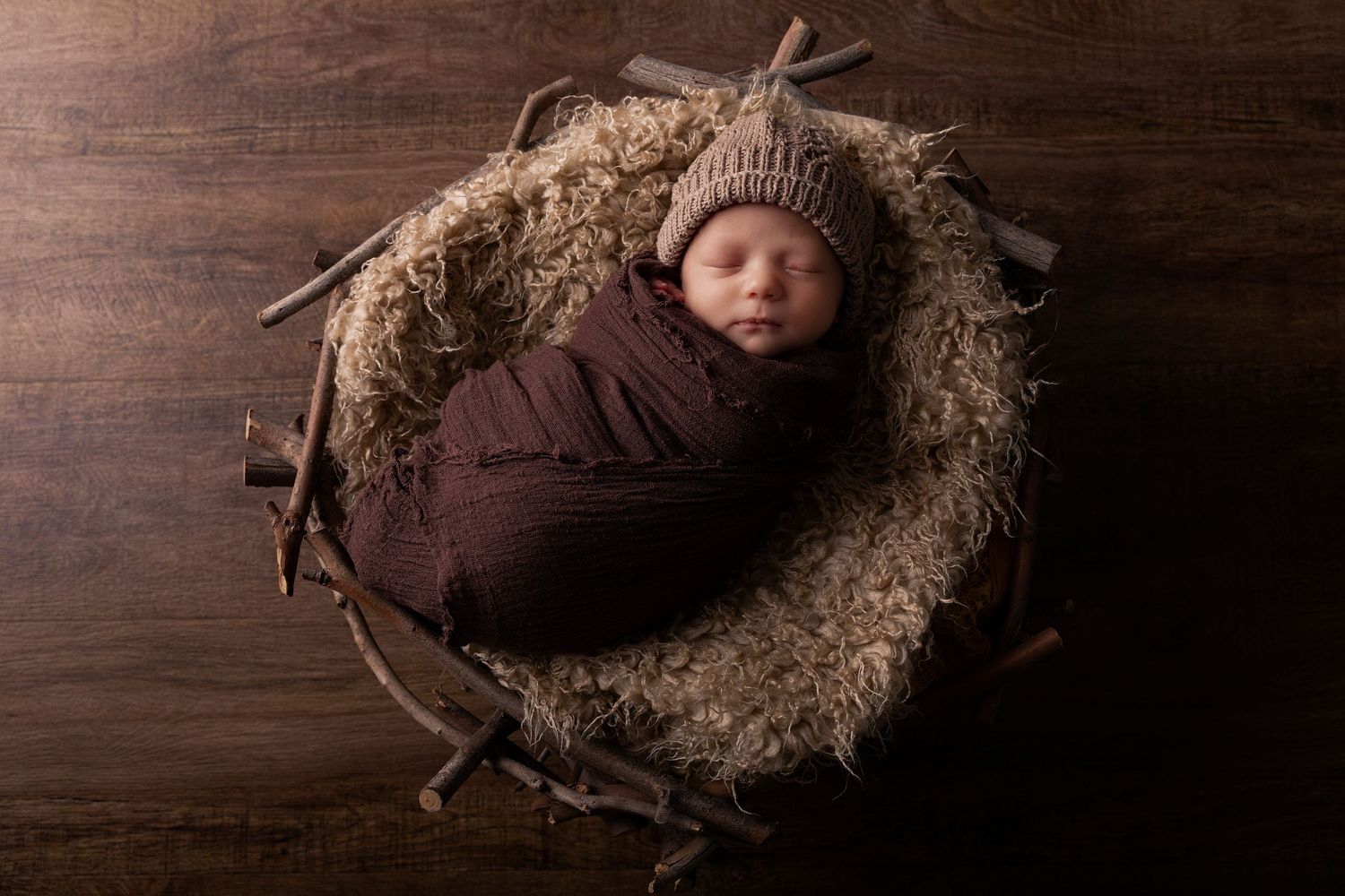 Newborn photography session with brown knit accessories and rustic wooden backdrop.