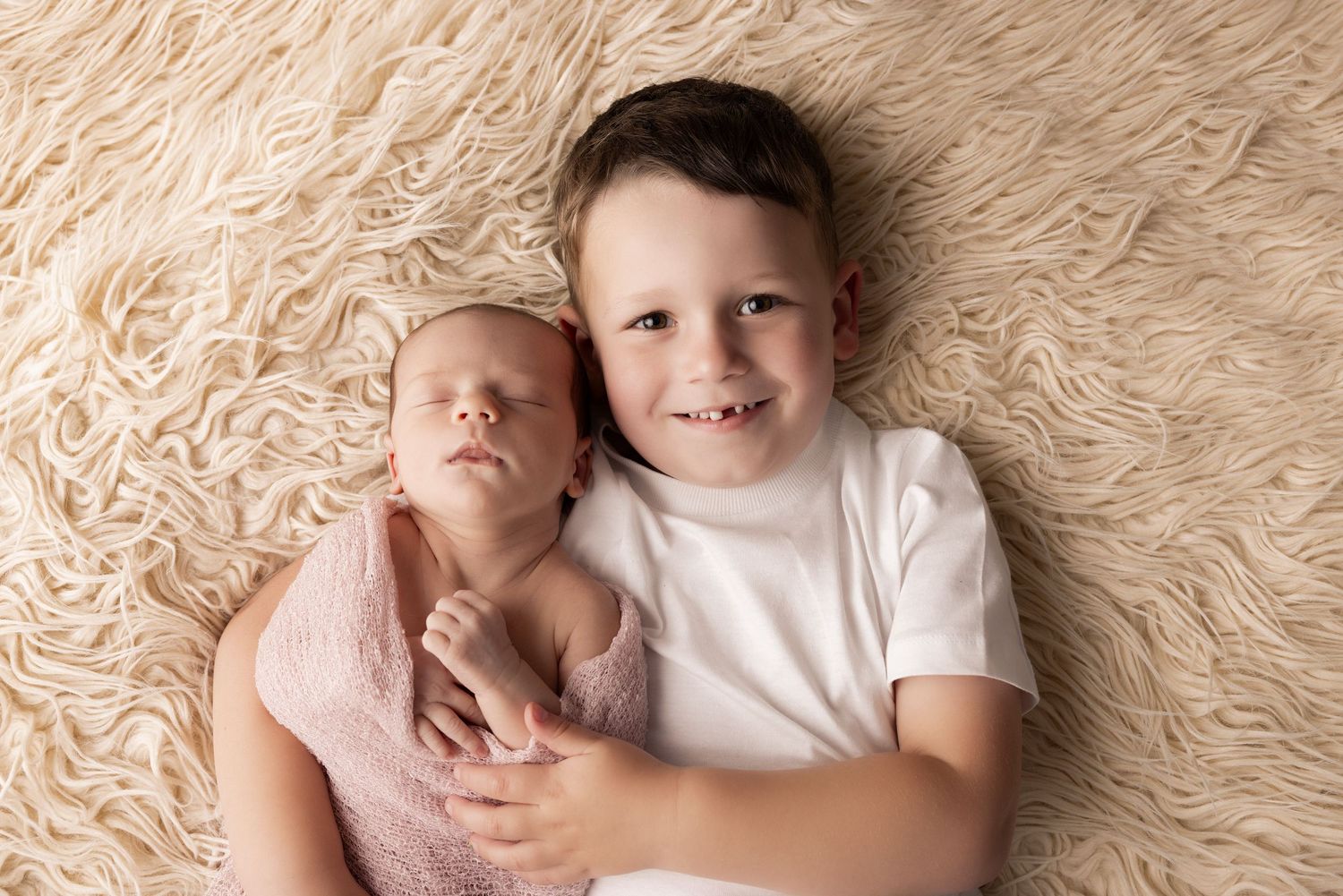 Sweet moment between siblings on cream furry backdrop.