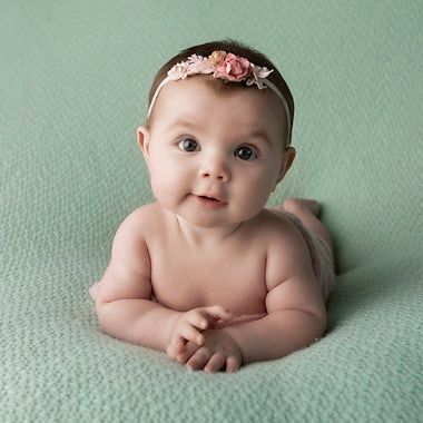 Infant wearing pink floral headband lying on mint green textured backdrop during professional photo session.