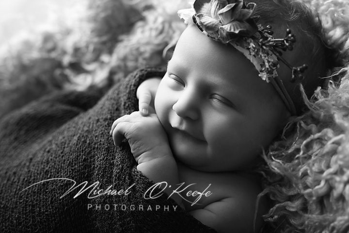 Black and white newborn photo of sleeping baby girl wearing floral headband by Michael O'Keefe Photography.