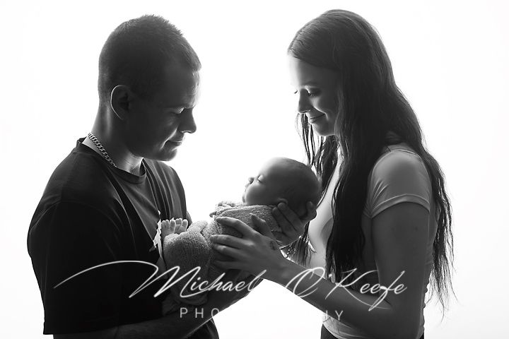 Black and white newborn photo of parents lovingly holding their sleeping baby, captured by Michael O'Keefe Photography.