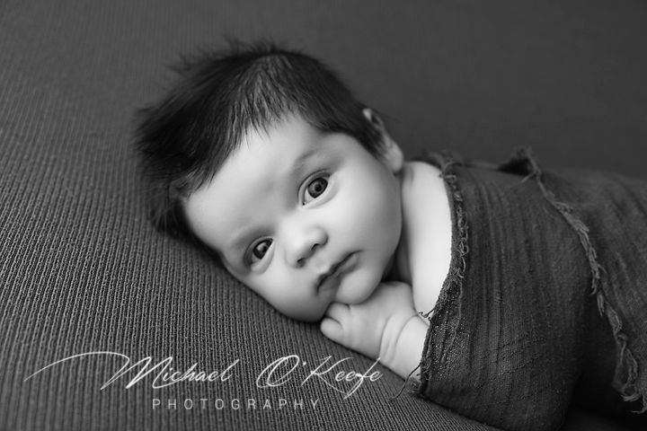 Black and white artistic portrait series showing different expressions and angles of a baby against a dark background.
