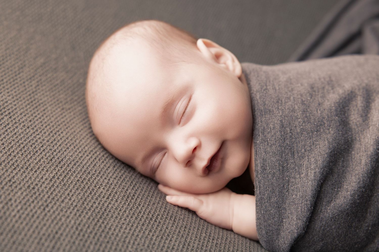 A sleeping baby in gray clothing rests peacefully against a soft gray background.