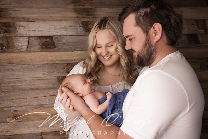 A couple shares a tender moment with their newborn baby against a rustic wooden wall backdrop.