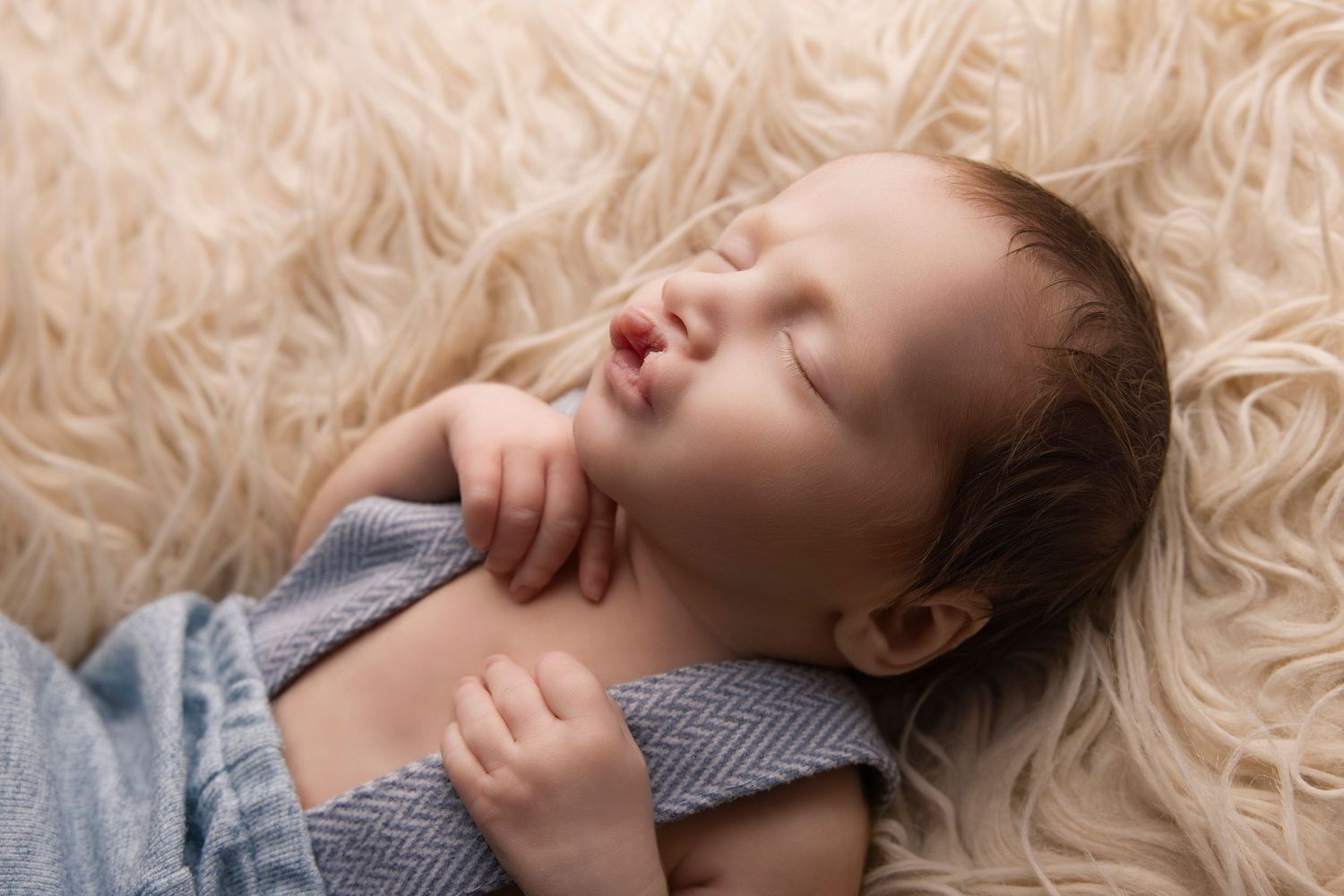 Baby sleeping peacefully on soft cream-colored fur rug in neutral tones.