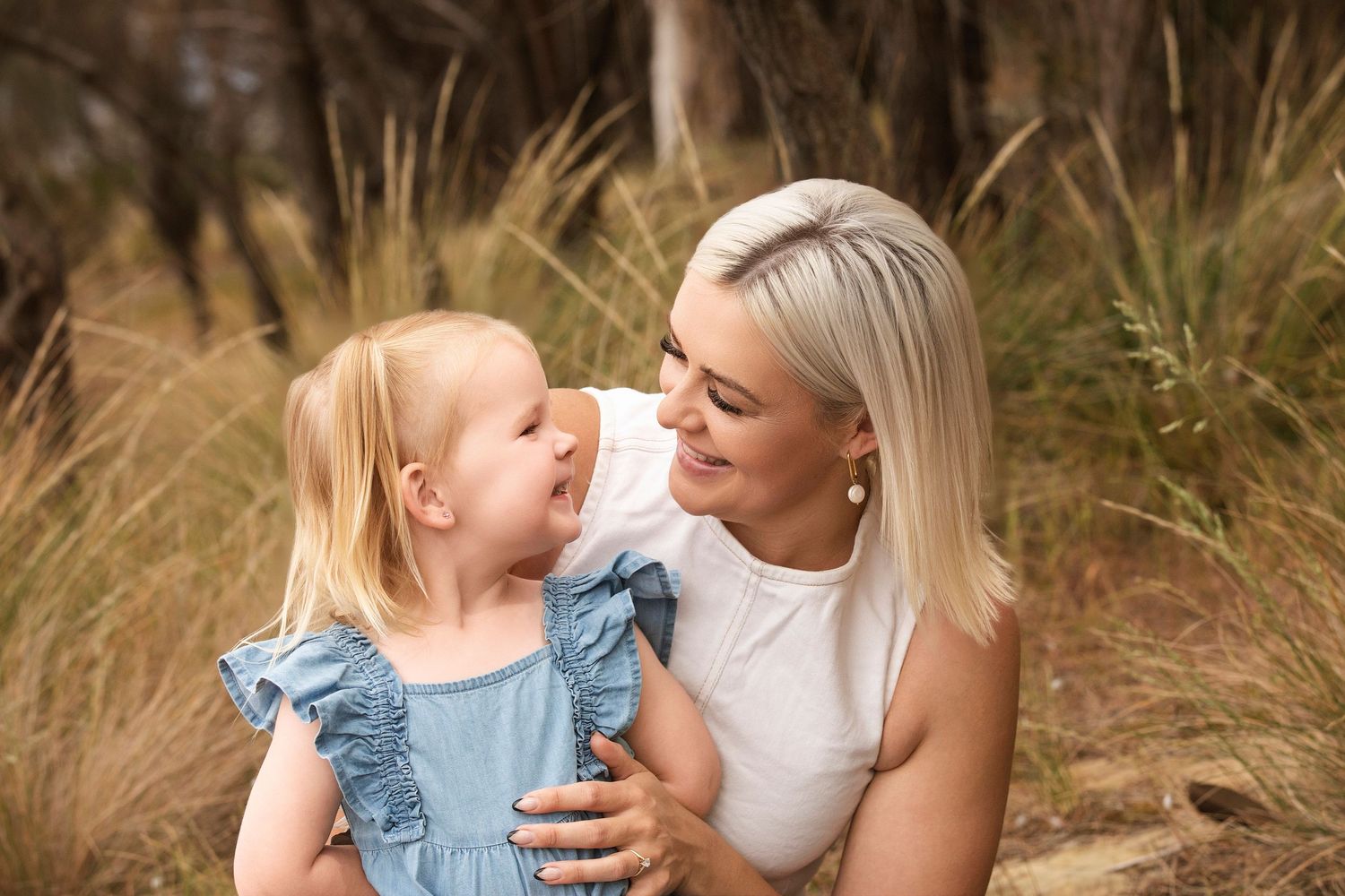 Mother and child share tender moments while sitting in tall grass during sunset.