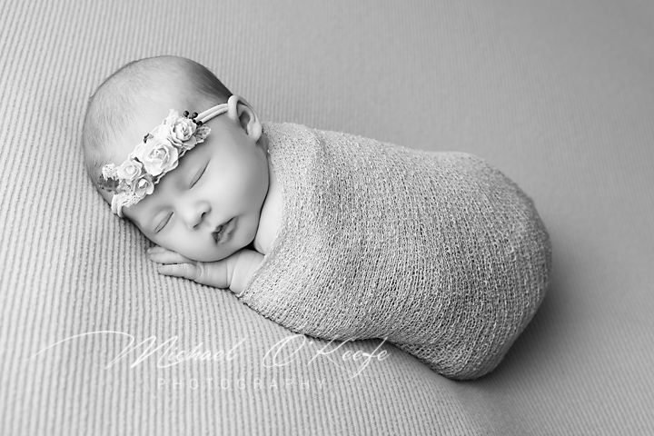Newborn baby wrapped in gray swaddle resting peacefully in artistic black and white portrait series.