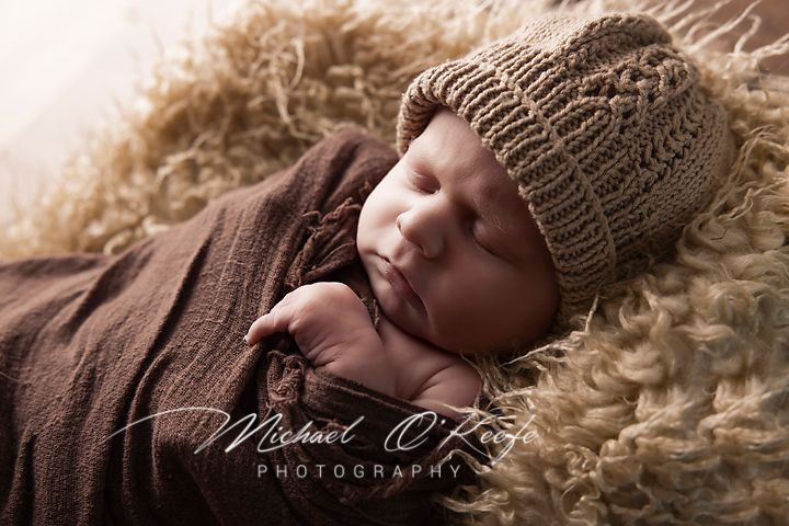 Sleeping baby wearing knit hat rests on textured cream fur blanket.