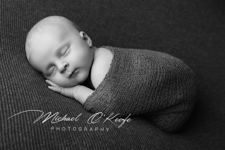 Black and white newborn photography by Michael O'Keefe, sleeping baby wrapped in knit blanket.