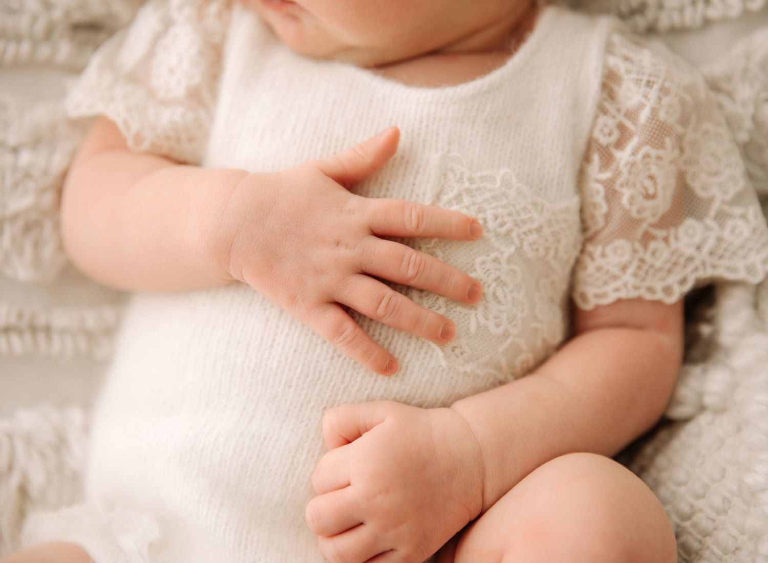 Close up of tiny newborn feet and delicate knit fabric against a white background.