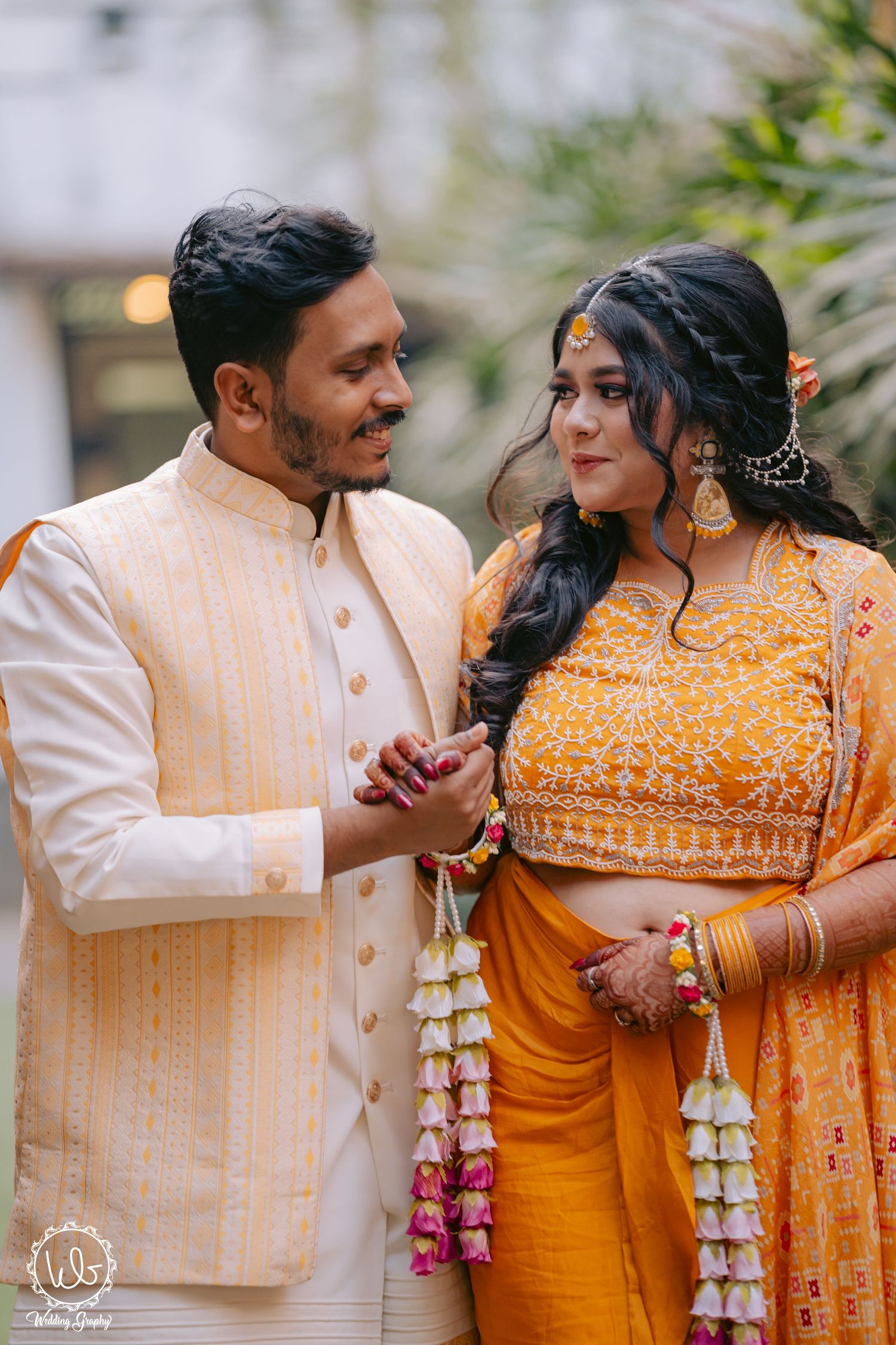 Couple in traditional South Asian attire sharing candid moments in orange and cream outfits.