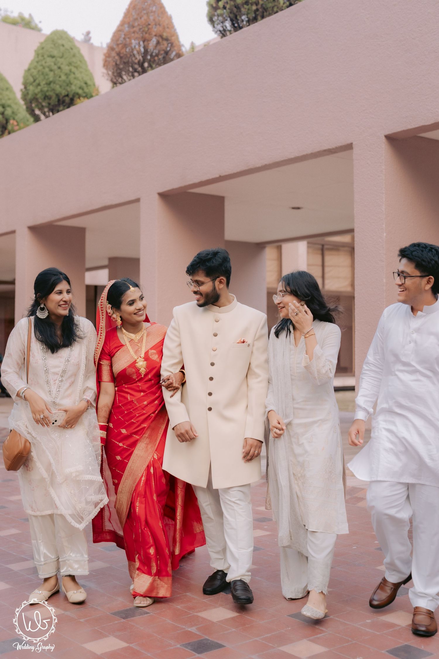 Wedding party members in white outfits and red attire pose playfully for photos.