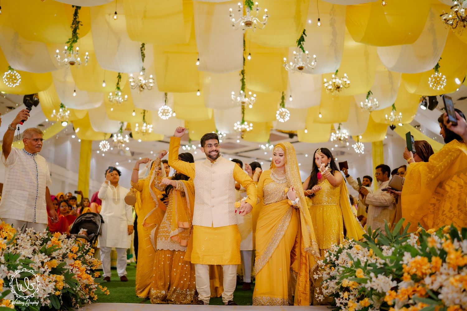 Wedding venue decorated in yellow theme with floral arrangements and hanging lights creating a warm ambiance.
