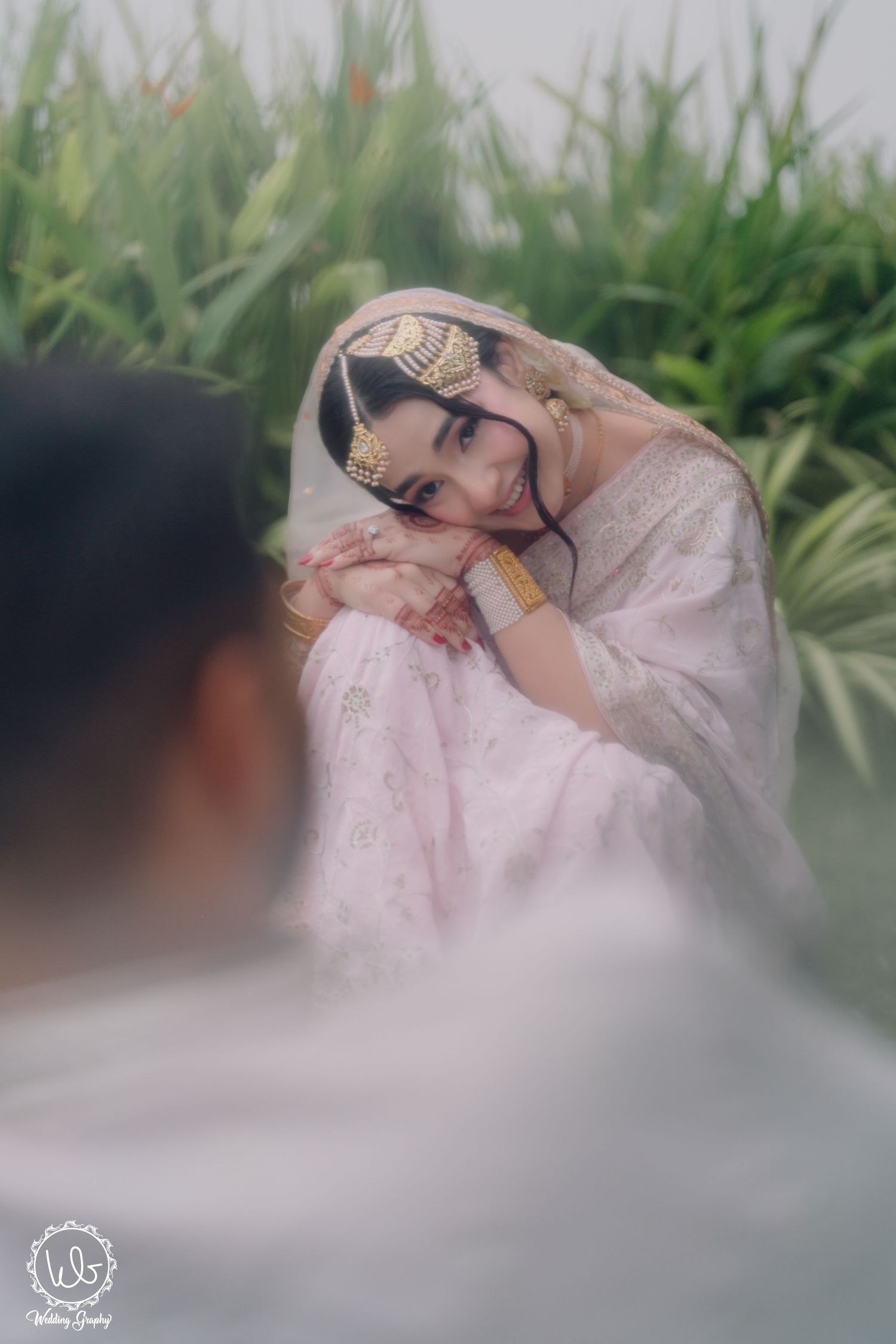 A dreamy portrait in soft focus shows someone in traditional white attire sitting among lush greenery.