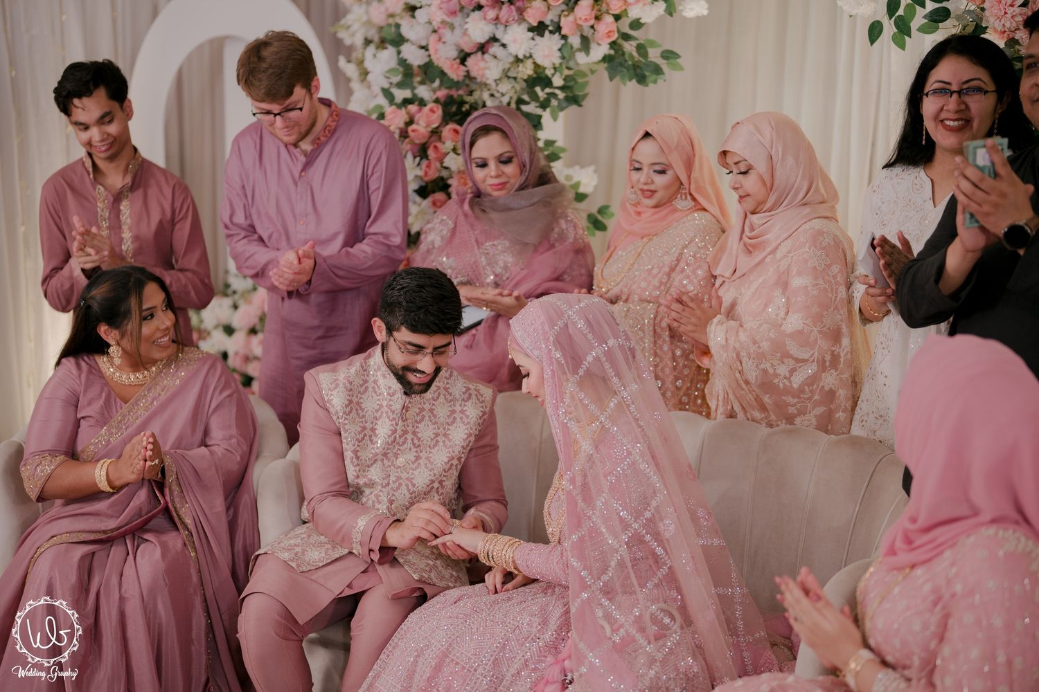 A wedding party poses together wearing coordinated pink and blush colored outfits at an elegant celebration.