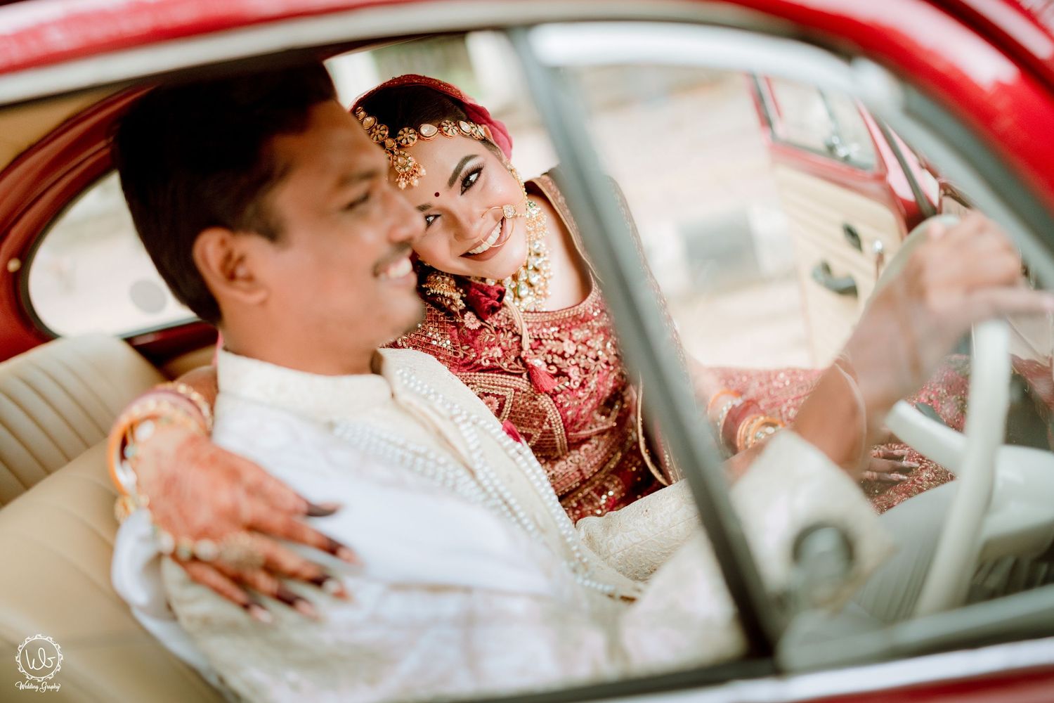 A couple shares a tender moment inside a vintage red car during their wedding celebration.