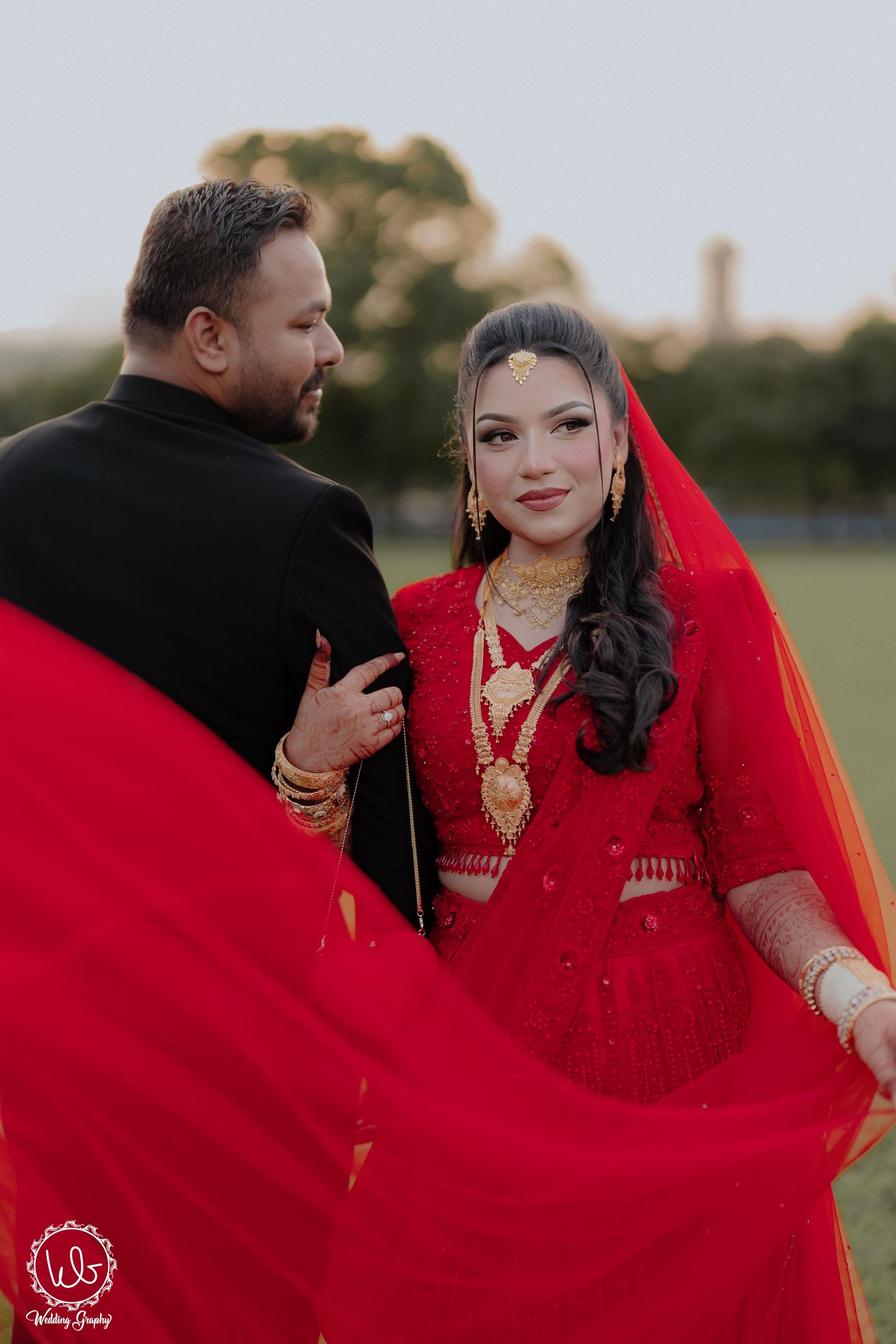 Romantic outdoor photoshoot featuring flowing red wedding attire against natural backdrop.