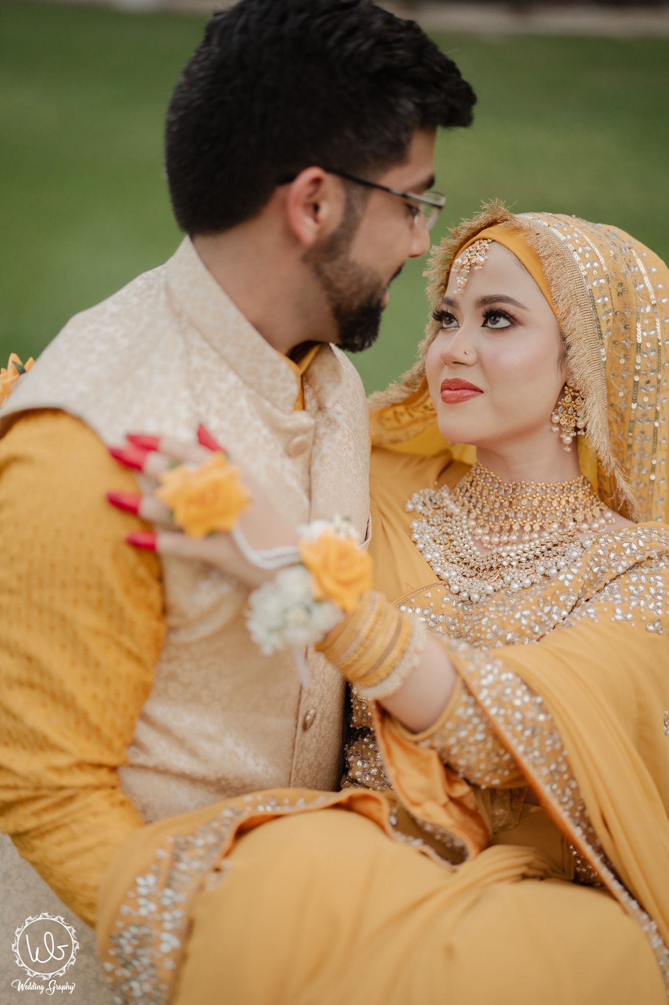 A couple in traditional South Asian wedding attire sharing an intimate moment in yellow and gold outfits.