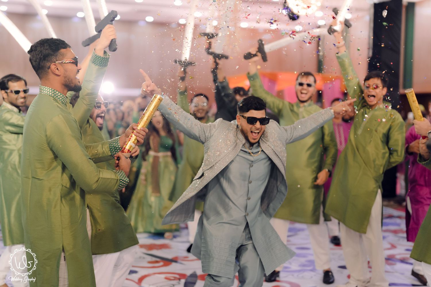 Groomsmen in olive green suits dancing and celebrating with confetti at a wedding reception.