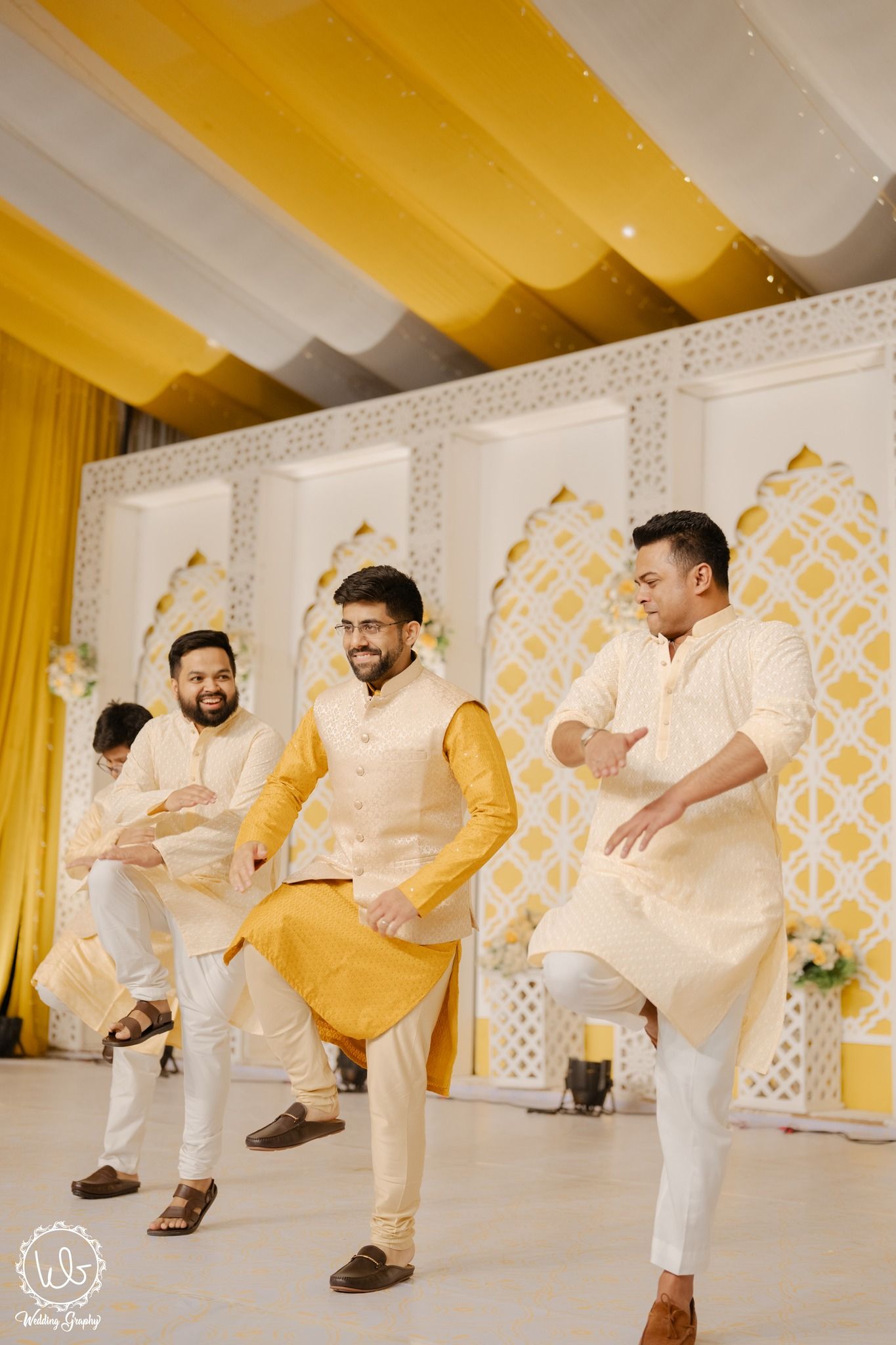A sequence of photos showing two people in white and yellow outfits performing a playful dance move against a patterned wall.