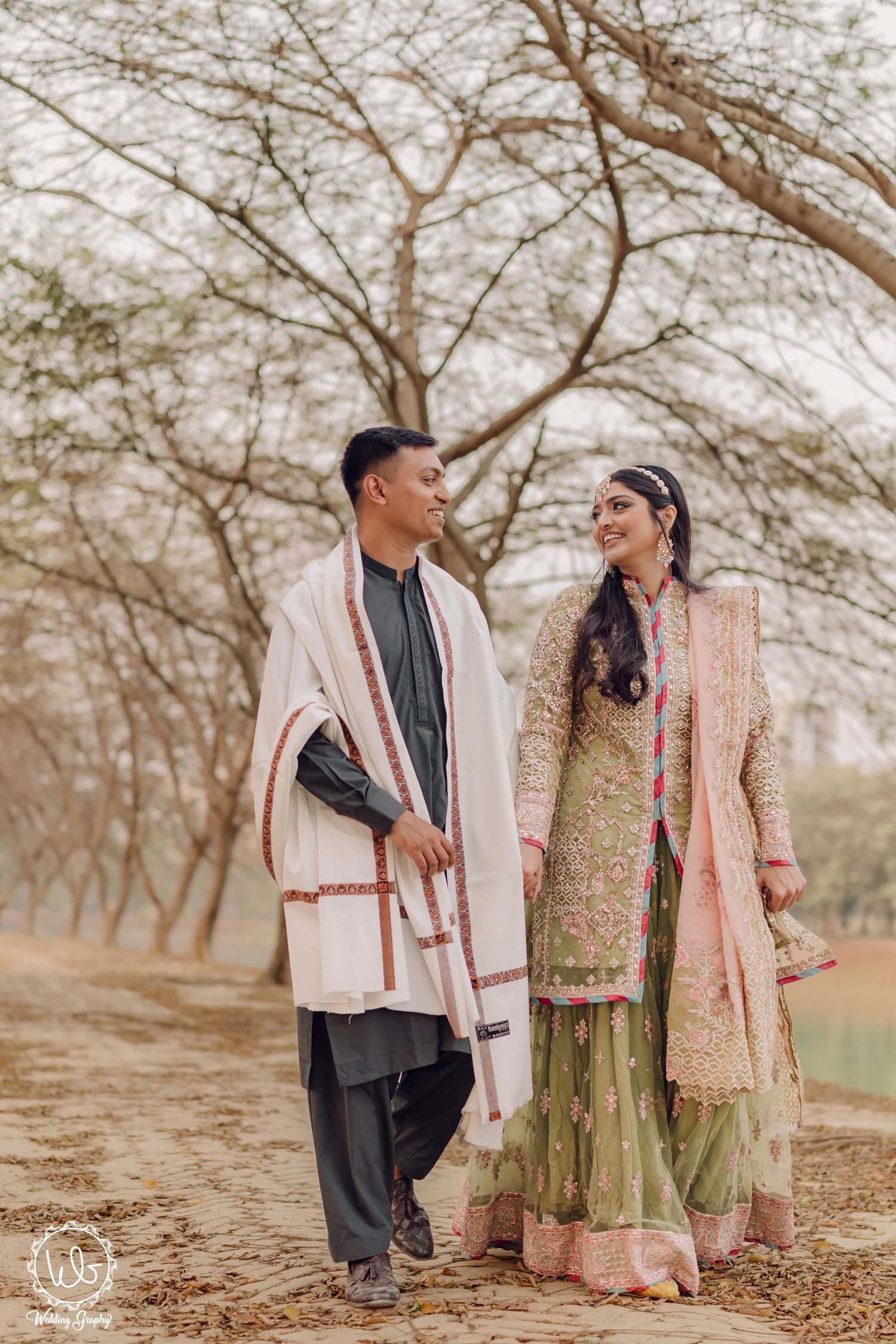 Romantic couple's photoshoot among bare trees wearing traditional South Asian formal attire.