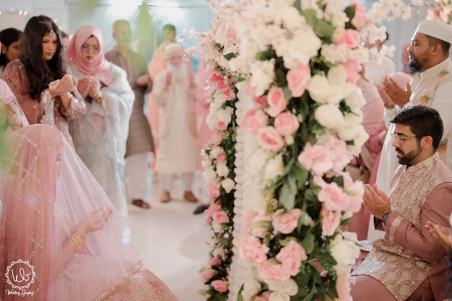 Elegant wedding celebration with pink and white floral arrangements as guests celebrate in traditional attire.