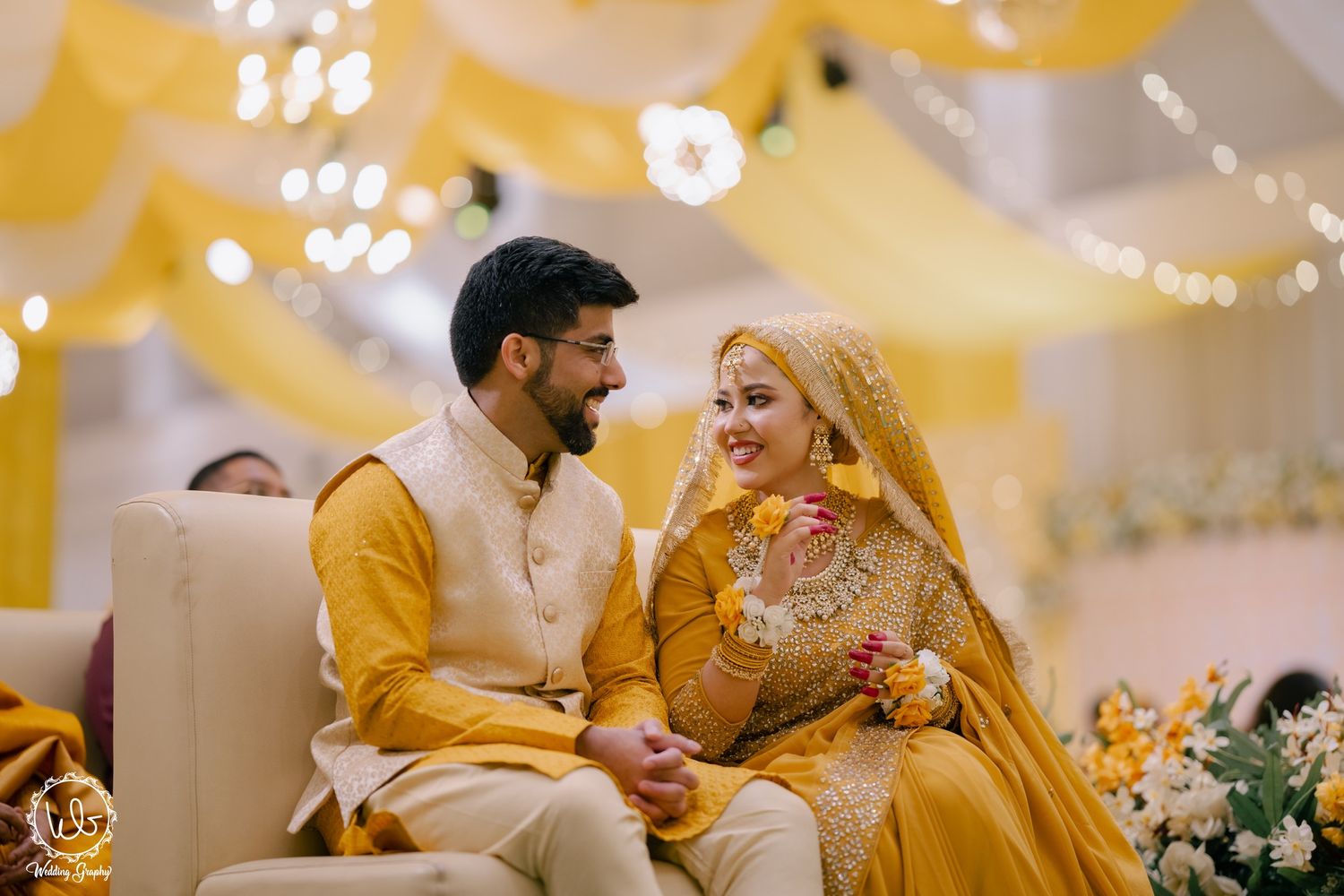 A couple in traditional yellow Indian wedding attire shares a joyful moment during their ceremony celebration.