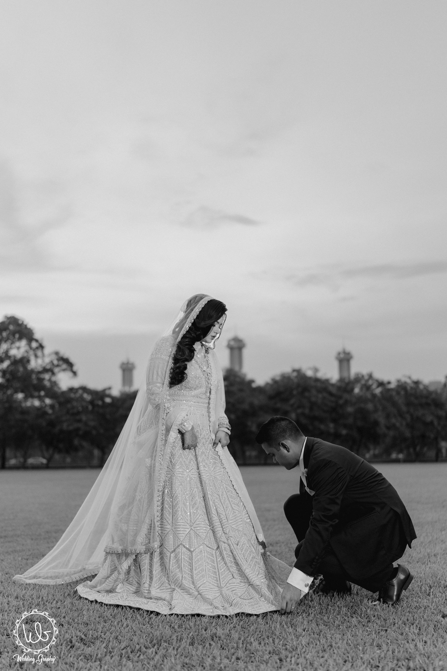 Black and white wedding photo on grassy field with dramatic sky.